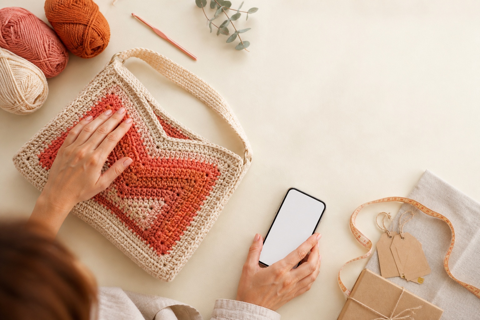 Bolsa de crochê, novelos e celular organizados sobre uma mesa de trabalho.